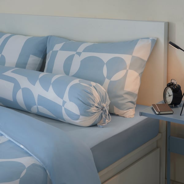Bed with blue bruinsvara linens; includes pillows, alarm clock, notebook, pen.