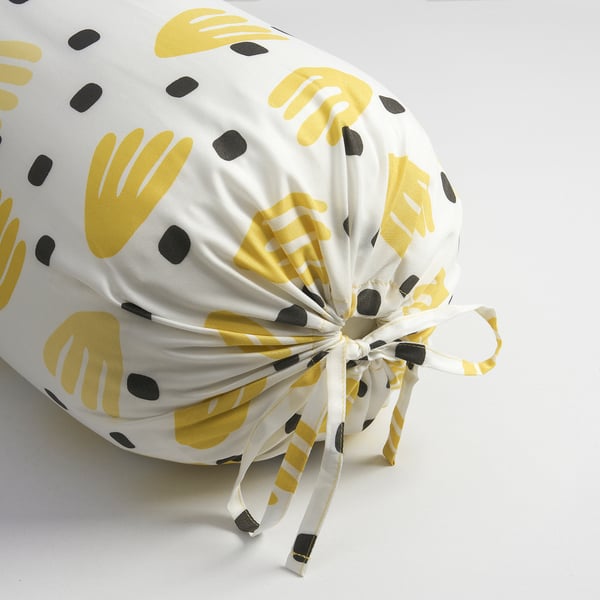 Decorative bolster pillow with yellow, black, and white tropical leaf pattern, tied with a bow.