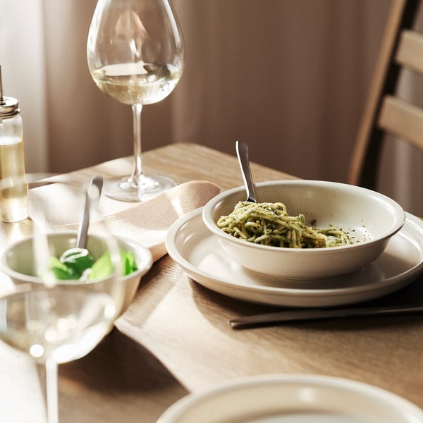 Rustic table setting with stoneware, food, and glass on wood table with chair.
