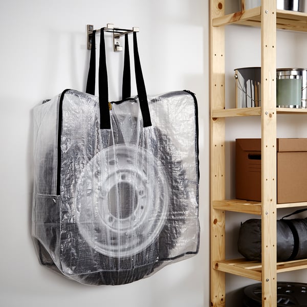 A large transparent storage bag hangs on a hook. It is durable, holds large items, and folds flat when empty.