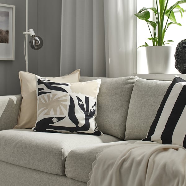 Modern living room with grey sofa, graphic centre cushion, striped & solid pillows, beige blanket, green plant, and lamp.