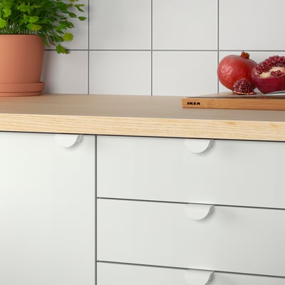 Wood countertop with white cabinets, featuring clip-on handles, and a pomegranate on a cutting board.