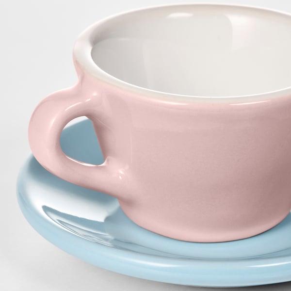 A pastel pink children’s mug sits on a light blue saucer, both smooth with even glazing.