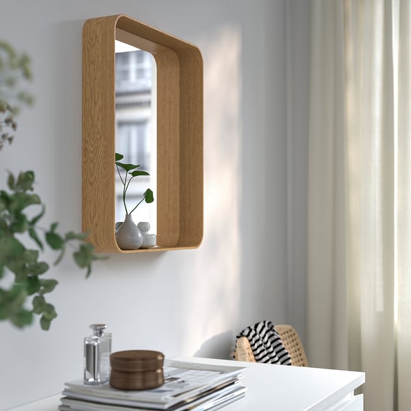 Wall mirror with shelf above desk for storage and decor.