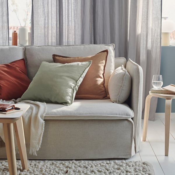 Cosy living room with grey-green linen cushions on a light-colored sofa, complemented by wooden side tables and a textured rug.