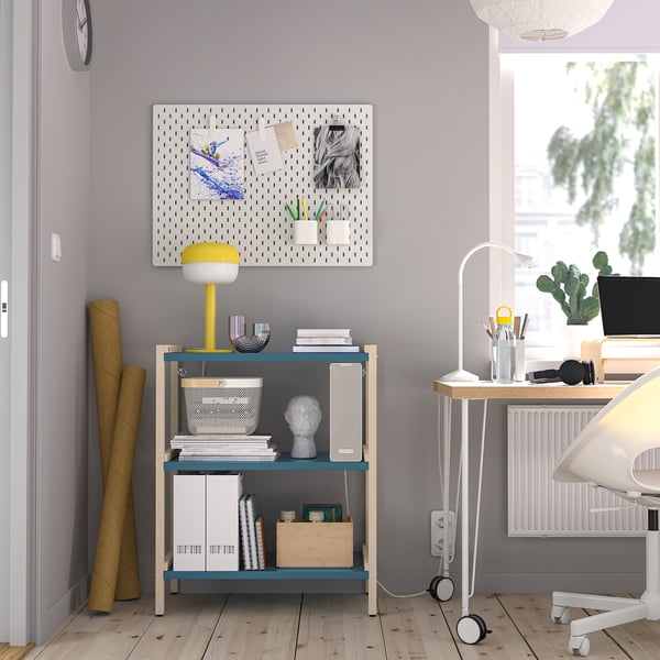 Home office with EKENABBEN shelves, books, decor, lamp, and pegboard. Light wood floor, purple walls, small desk by window with cactus and computer.
