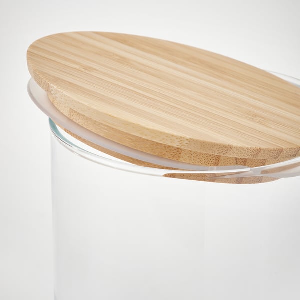 Displays a kitchen storage jar with a bamboo lid and transparent glass body, designed for storing dry foods.