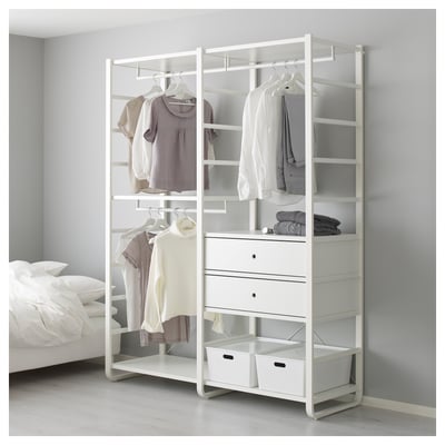 Modern ELVARLI wardrobe with open shelves, hanging rods, and drawers, displaying neatly organised clothes beside a bed.