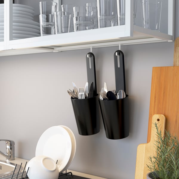 Black hooks hang from white cabinet, holding utensils. Below, a dish drainer holds plates next to a wooden cutting board.