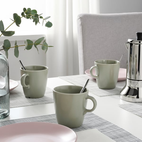 Table set with two green mugs, pink plates, and a water carafe with flowers. A coffee maker sits beside the mugs.