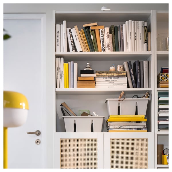 White bookshelf with colourful books, decorative boxes, and a yellow lamp.