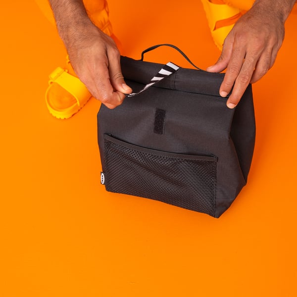 Person holding black insulated FRAMTUNG lunch bag; sleek, water-resistant, mesh pocket.