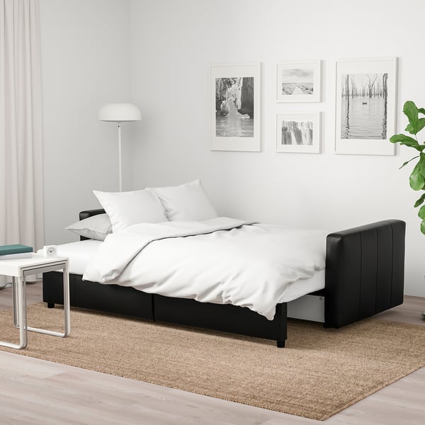 Black sleeper sofa with white bedding, photos, and lamp on rug.