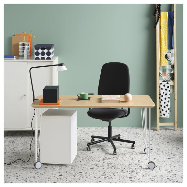 Home office with light wood desk, black chair, lamp, and green wall shelves.