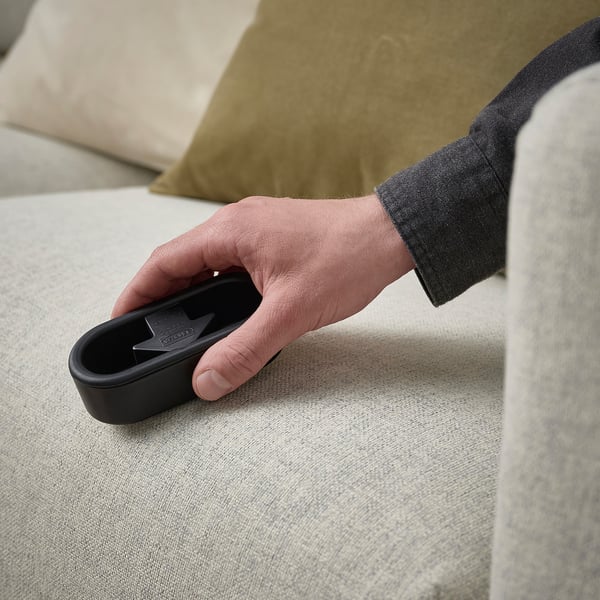 A hand holds a lint brush on a couch. The brush removes hair and lint from clothes and surfaces. Simple and reusable for quick cleaning.