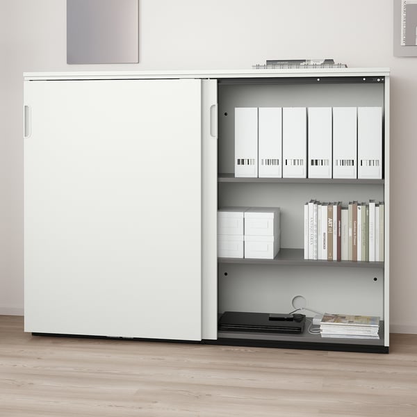 White storage cabinet with sliding doors, adjustable shelves holding files and books, and a lock for security.