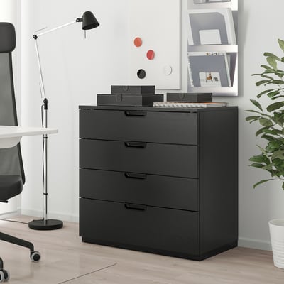 Modern black GALANT chest with 5 drawers sits in stylish office. Its sleek design complements white desk and shelves, providing ample storage space.