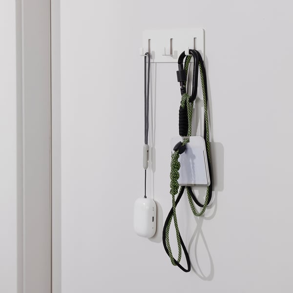 Self-adhesive wall rack with hooks holding items, including a white power bank and a black and yellow chord.