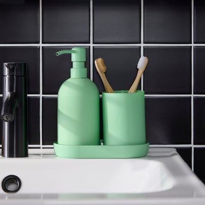Green glass soap dispenser and toothbrush holder with tray on sink, modern bathroom decor.