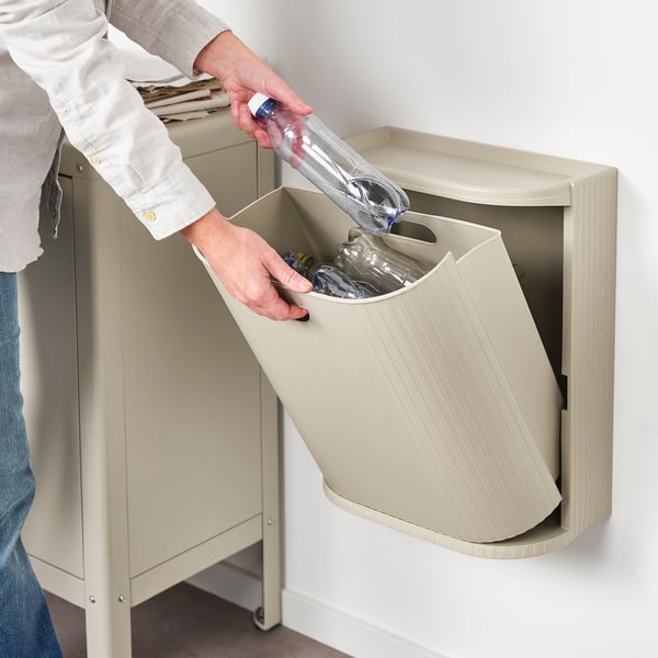 Person disposes empty water bottle into a wall-mounted, beige recycling bin, showcasing its accessibility and ease of use.