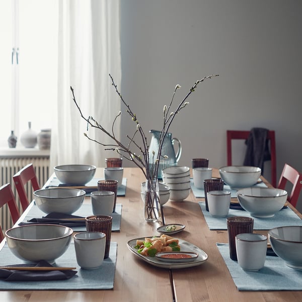Sandy-glazed GLADELIG tableware set on rustic table with red chairs and branch centrepiece.