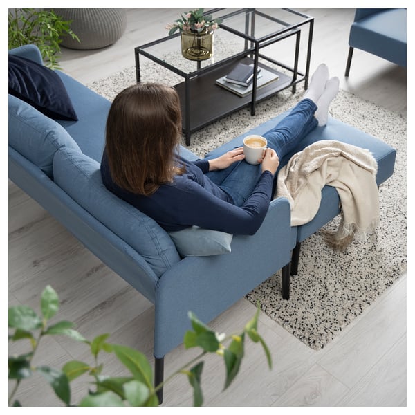 Person on blue GLOSTAD sofa enjoying coffee. Modern design with soft cushions and blanket.