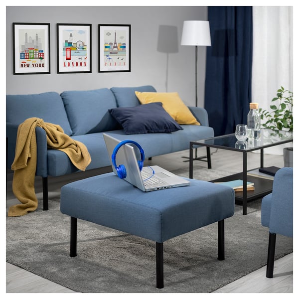 Cosy blue living room with GLOSTAD sofa and matching footstool. Laptop and headphones on the stool.