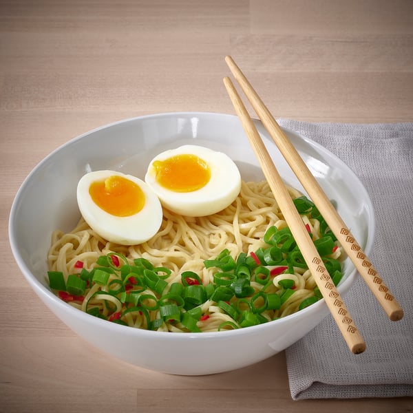 A bowl of noodles with chopped scallions and a halved boiled egg, served with chopsticks.