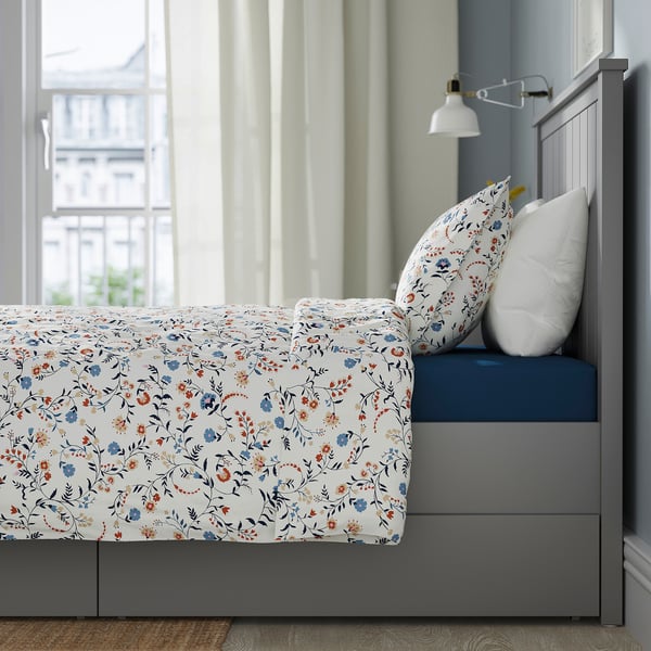 Bed with floral duvet and pillows, grey frame, built-in storage drawers, and headboard.