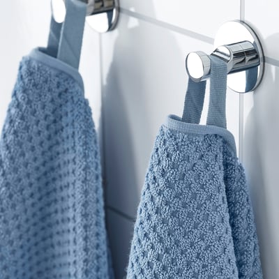 Two blue towels hang neatly on chrome hooks, showcasing their soft, absorbent texture and sturdy cotton material.