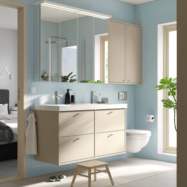 Modern light blue tiled bathroom with HAVBÄCK beige wall cabinet and mirrored cabinet above double sink, toilet, and plant.