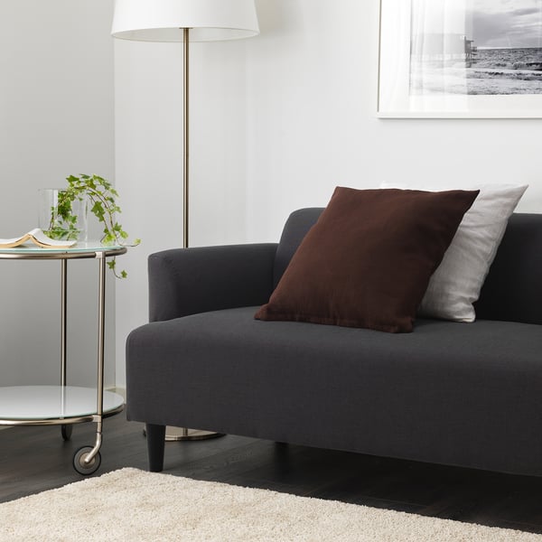 Grey HEMLINGBY sofa with pillows, side table with plant and book, wall lamp and photo.