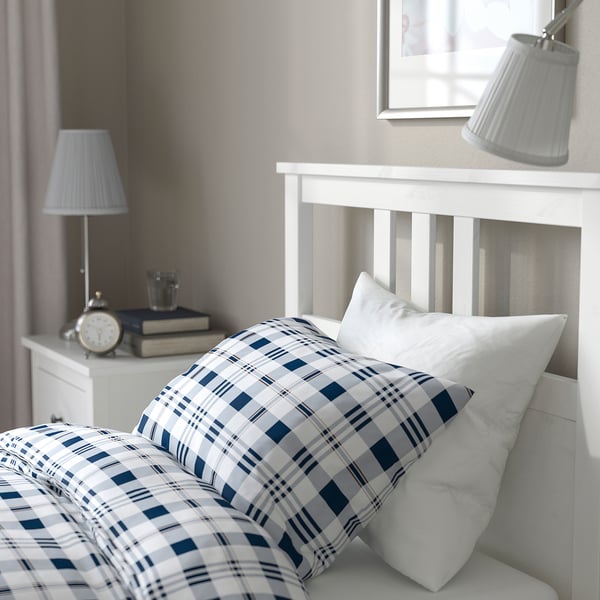 Cosy bed with checked bedding, 2 lamps, a clock, and books on a bedside table, showing comfort and organisation.