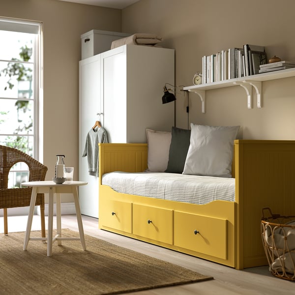 Cosy bedroom with HEMNES yellow daybed, white shelves, wicker chair, and table.