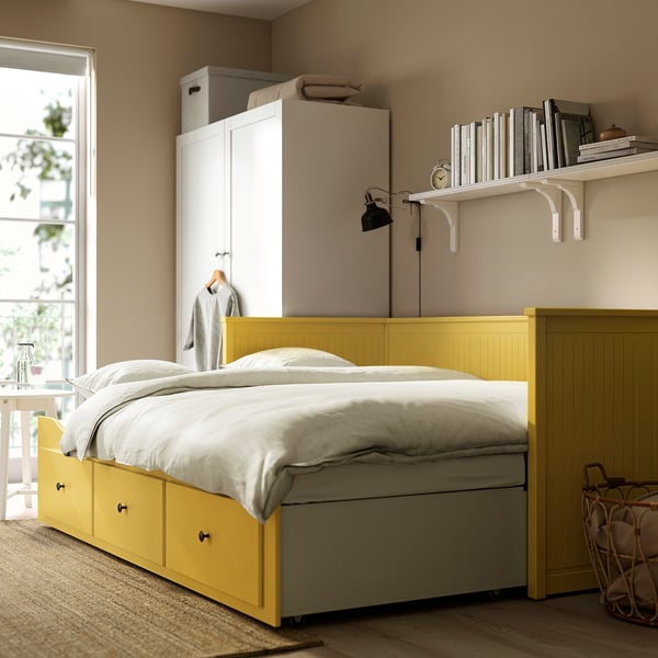 Bright yellow HEMNES day-bed contrasting against neutral bedroom decor with large storage drawers; fits perfectly under a tall, narrow bookshelf.