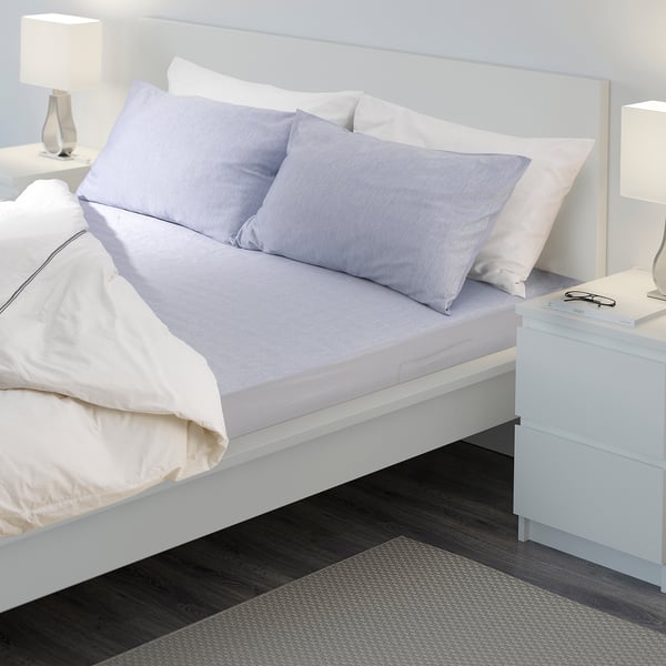 Bed with white and light blue linens, two lamps, and a book on a bedside table.