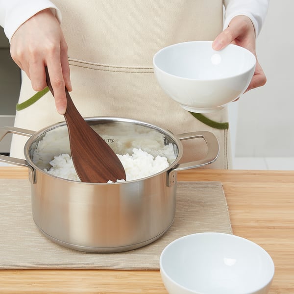 Person serving rice with wooden spoon, wearing apron.