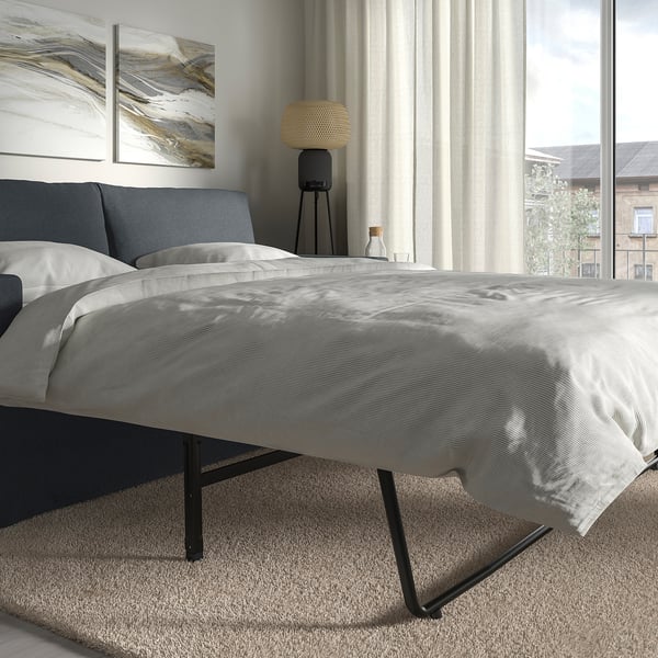 Modern bedroom with HYLTARP sofa-bed, reversible cushions, large window, sheer curtains.