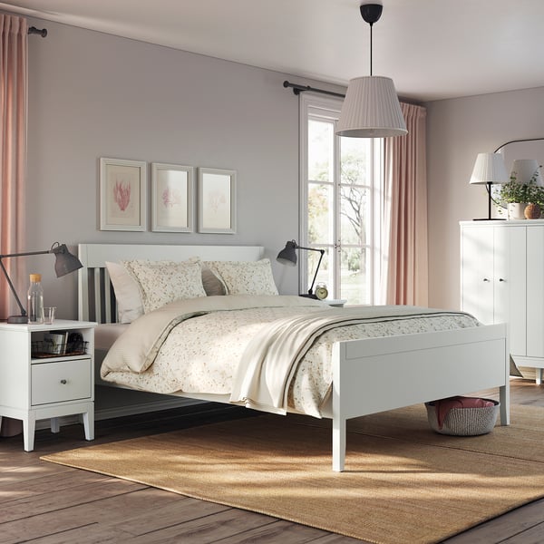 Cosy bedroom with white IDANÄS bed, beige linens, black lamps, wooden floor, and pink curtains.