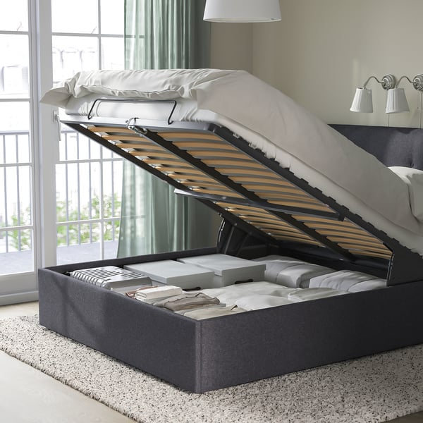 Ottoman bed with lift-up base for under-bed storage. Upholstered headboard, dark grey fabric, slatted base.