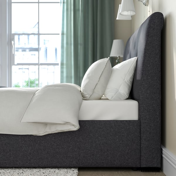 A grey upholstered bed with a sloping headboard, white pillows, and a cosy blanket. It under-bed storage and a lift mechanism.