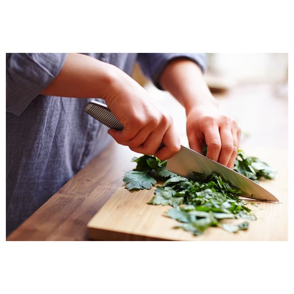 Person chops herbs on wooden board with stainless knife.