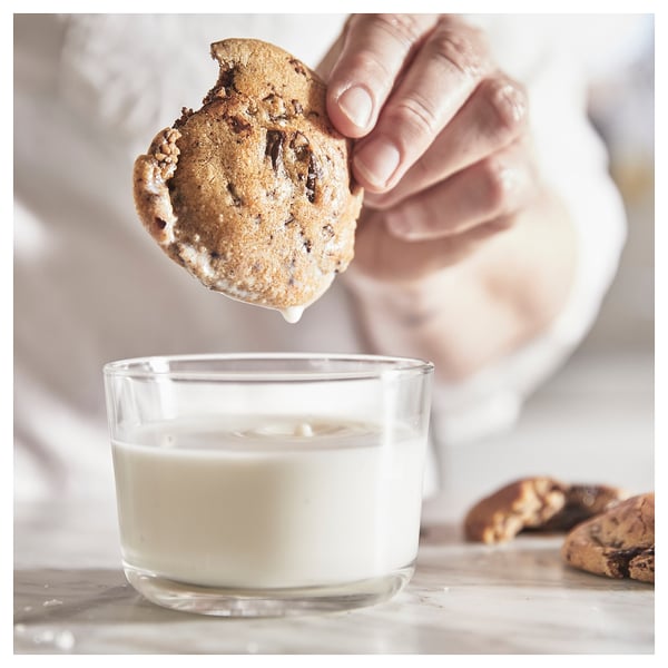 Hand dipping chocolate chip cookie into clear glass of milk. Simple, classic scene showcasing a timeless glass design.