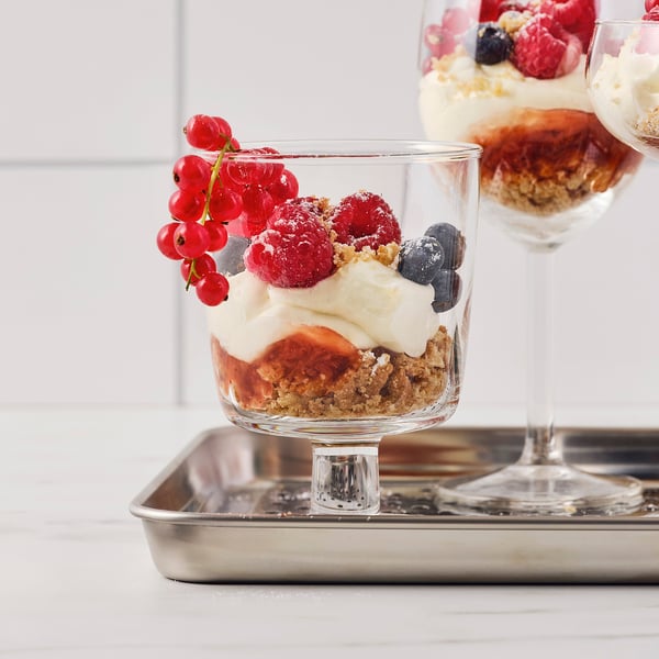 Glass dessert bowl with fruit and cream, on a stainless steel tray.