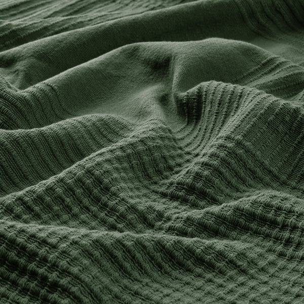 Dark green woven cotton bedspread, texture visible, waves & folds shown.
