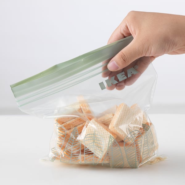 Hand seals clear plastic bag labeled ikea containing snacks. Product: ISTAD.