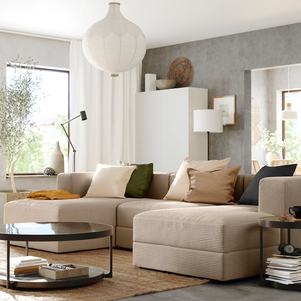 Modern living room with beige JÄTTEBO sectional sofa, colourful pillows, round coffee table, large window, white curtains, and hanging lamps.
