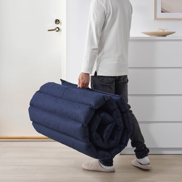 Person carrying rolled-up blue futon mattress, showing ease of transport and storage.