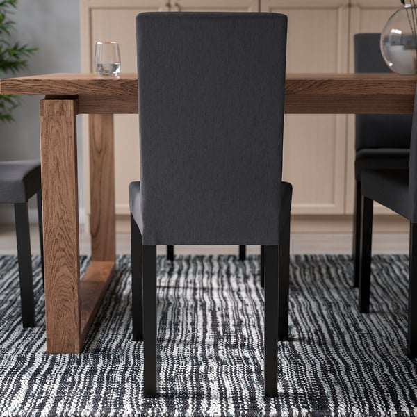 Modern dining chair with high, dark fabric back and seat, wooden legs, in minimalist setting.