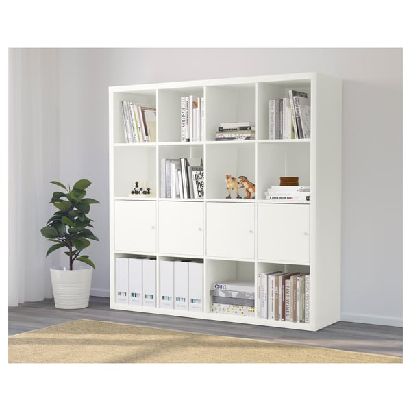 White KALLAX shelving unit holding books, decorative items, and filing folders, with a potted plant nearby.